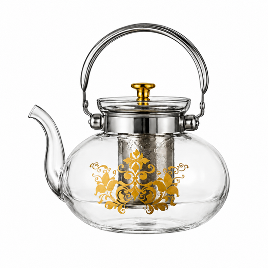 Clear glass teapot with a silver metal handle and lid, featuring a gold-toned decorative damask pattern on the front and a gold-toned lid knob.